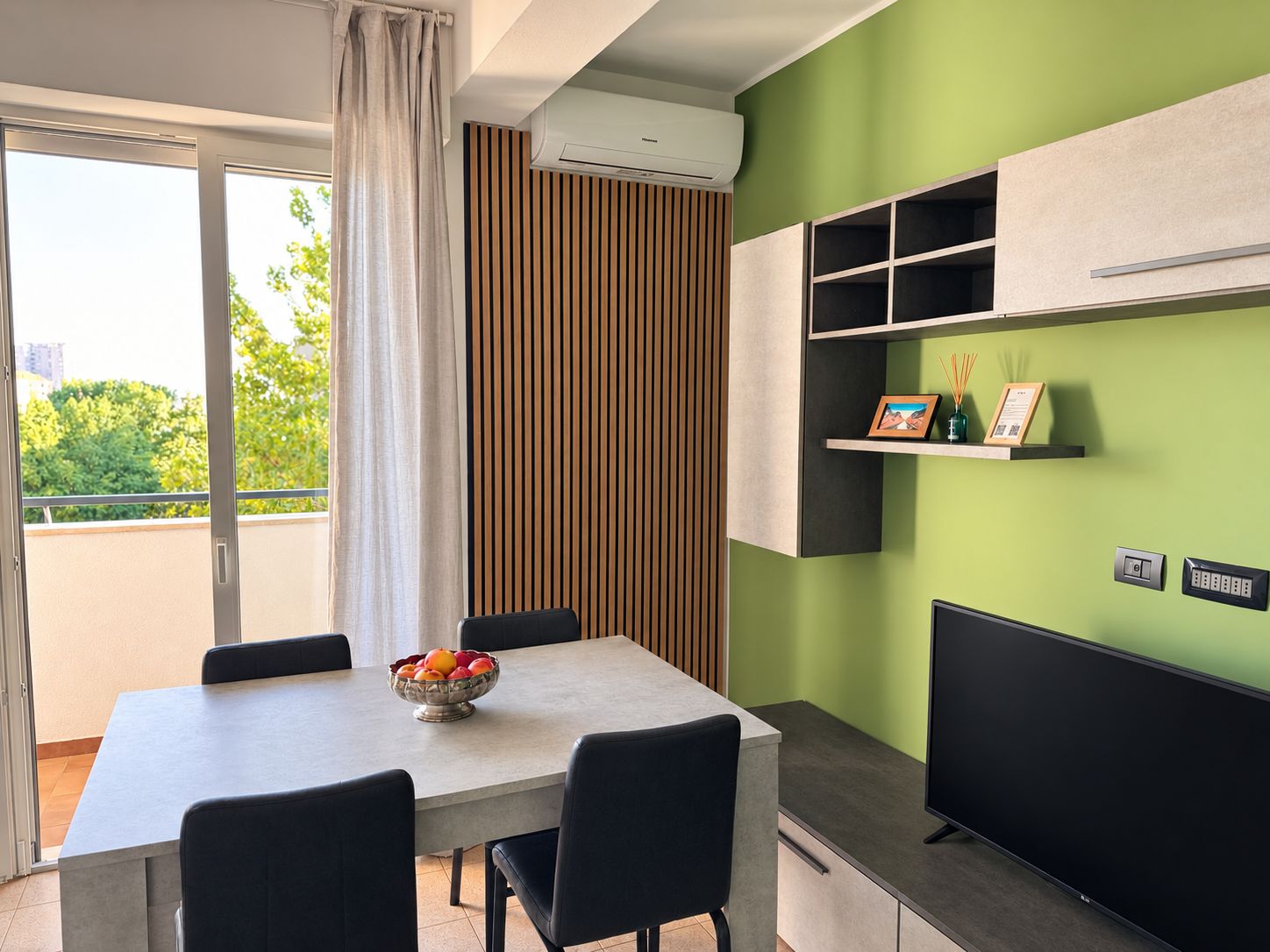 A modern kitchen with a dining area, a built-in TV, and a view through the window.
