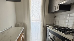 A kitchen with a stove, oven, and cabinets, a window with a curtain, and a radiator. - Strategic two-room apartment: M2 Metro, Navigli and Forum (Milano)
