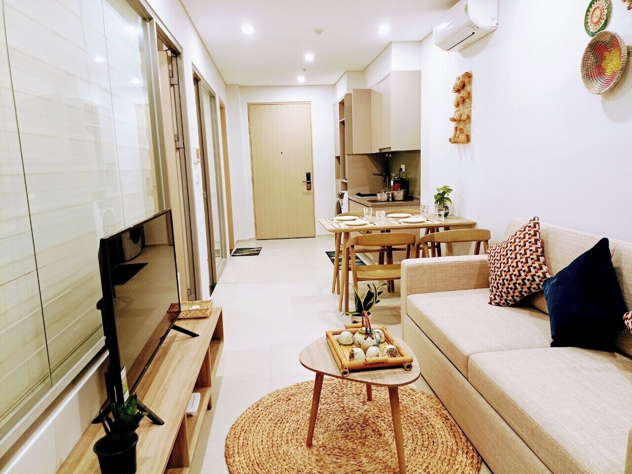 Una sala moderna con un televisor de pantalla plana, un sofá, una mesa de comedor y una cocina al fondo.