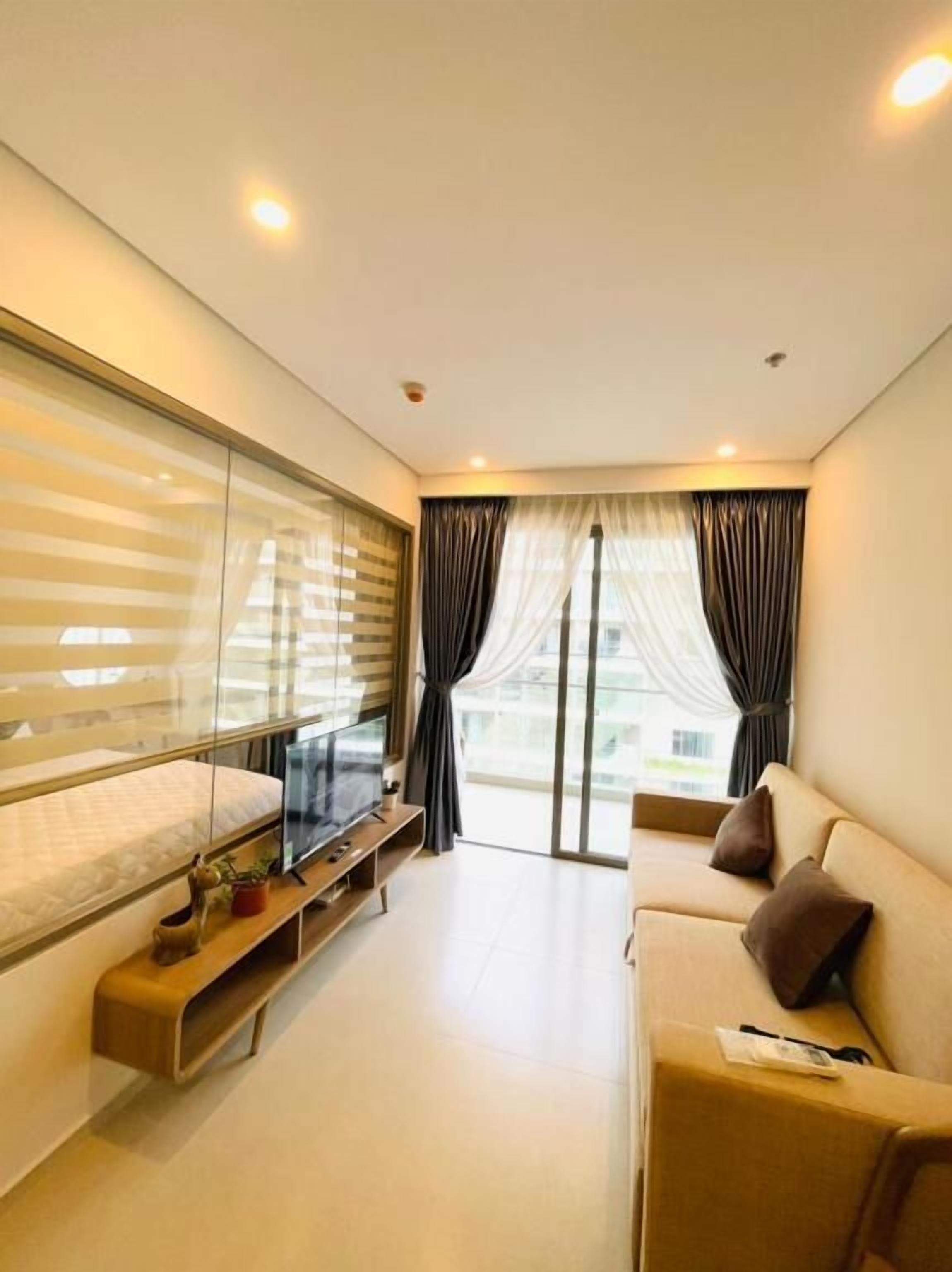 A modern hotel room with a bed, a TV, a sofa, and a balcony with curtains.
