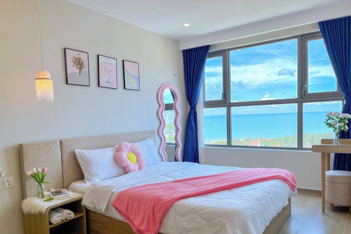 Un dormitorio con cama, una mesita de noche con un florero, una ventana con vistas y un espejo.