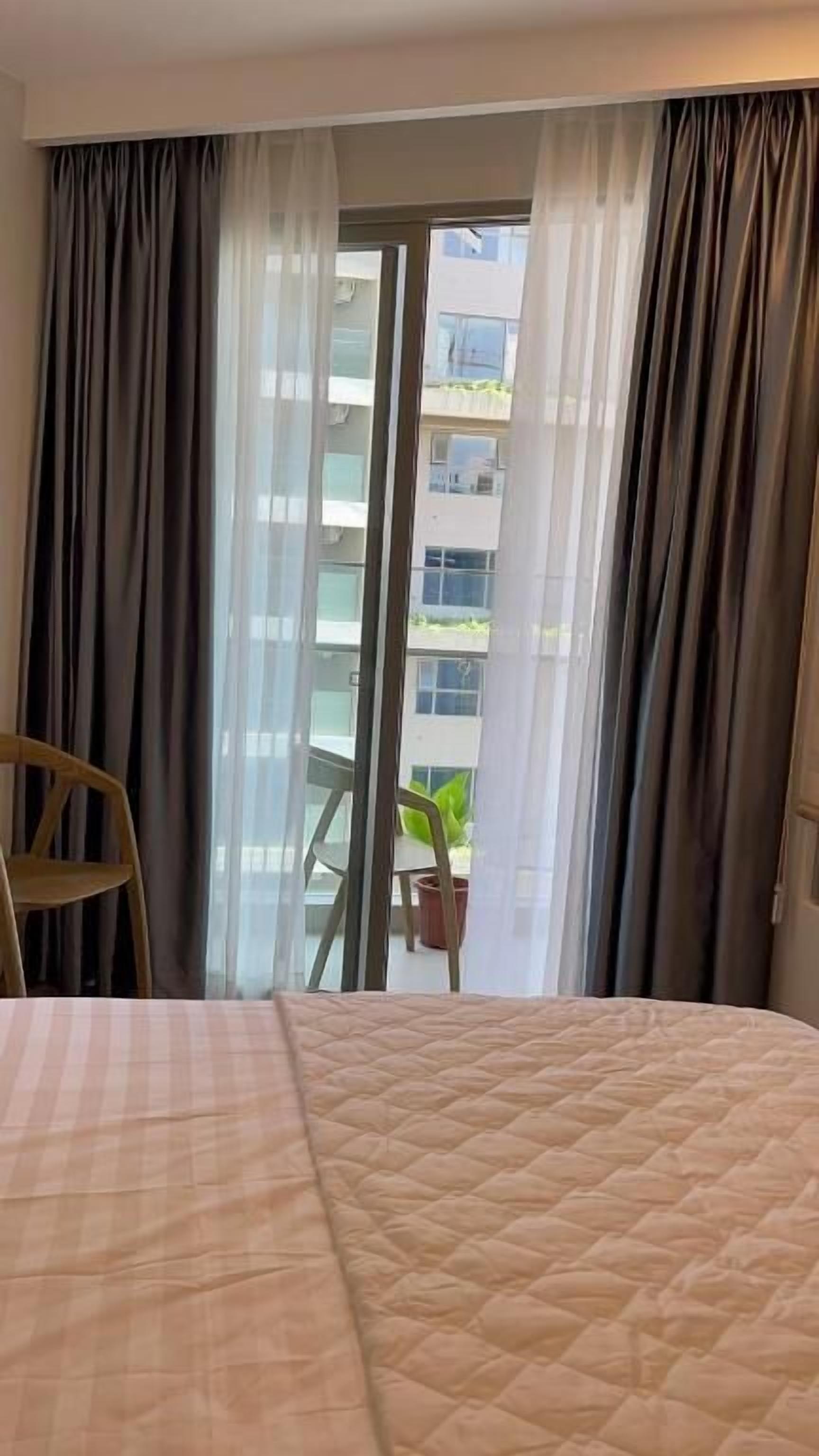 A hotel room with a bed, a chair, and a view of a building through a glass door.