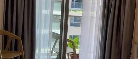 A hotel room with a bed, a chair, and a view of a building through a glass door.