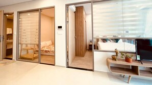 Een moderne hotelkamer met een schuifglazen deur naar een balkon, een bed met een witte dekbedovertrek, een bureau met een laptop en een kleine potplant.