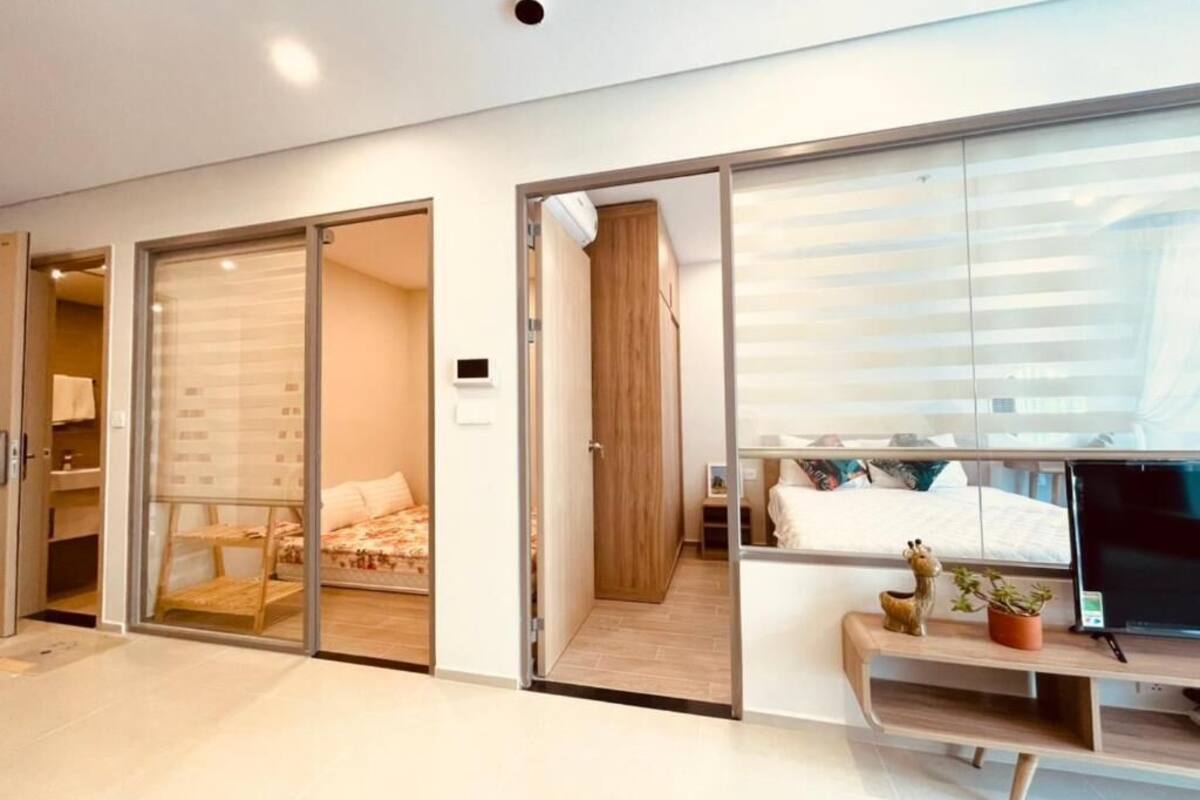 Una habitación de hotel moderna con un puerta corrediza de vidrio que da a un balcón, una cama con cubrecama blanco, un escritorio con una computadora portátil y una pequeña planta en maceta.