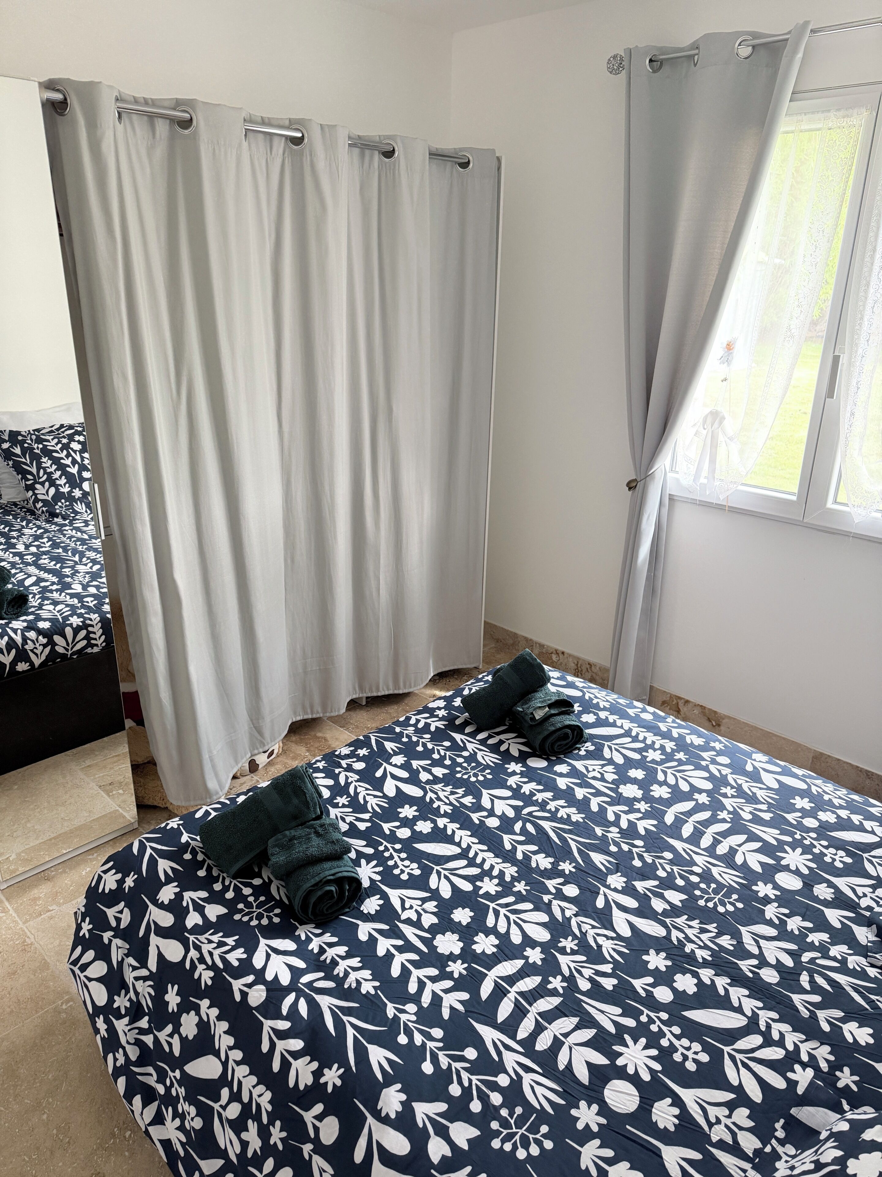 A bedroom with two beds, a window with a view, and a bathroom with a shower curtain.
