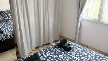 A bedroom with two beds, a window with a view, and a bathroom with a shower curtain.