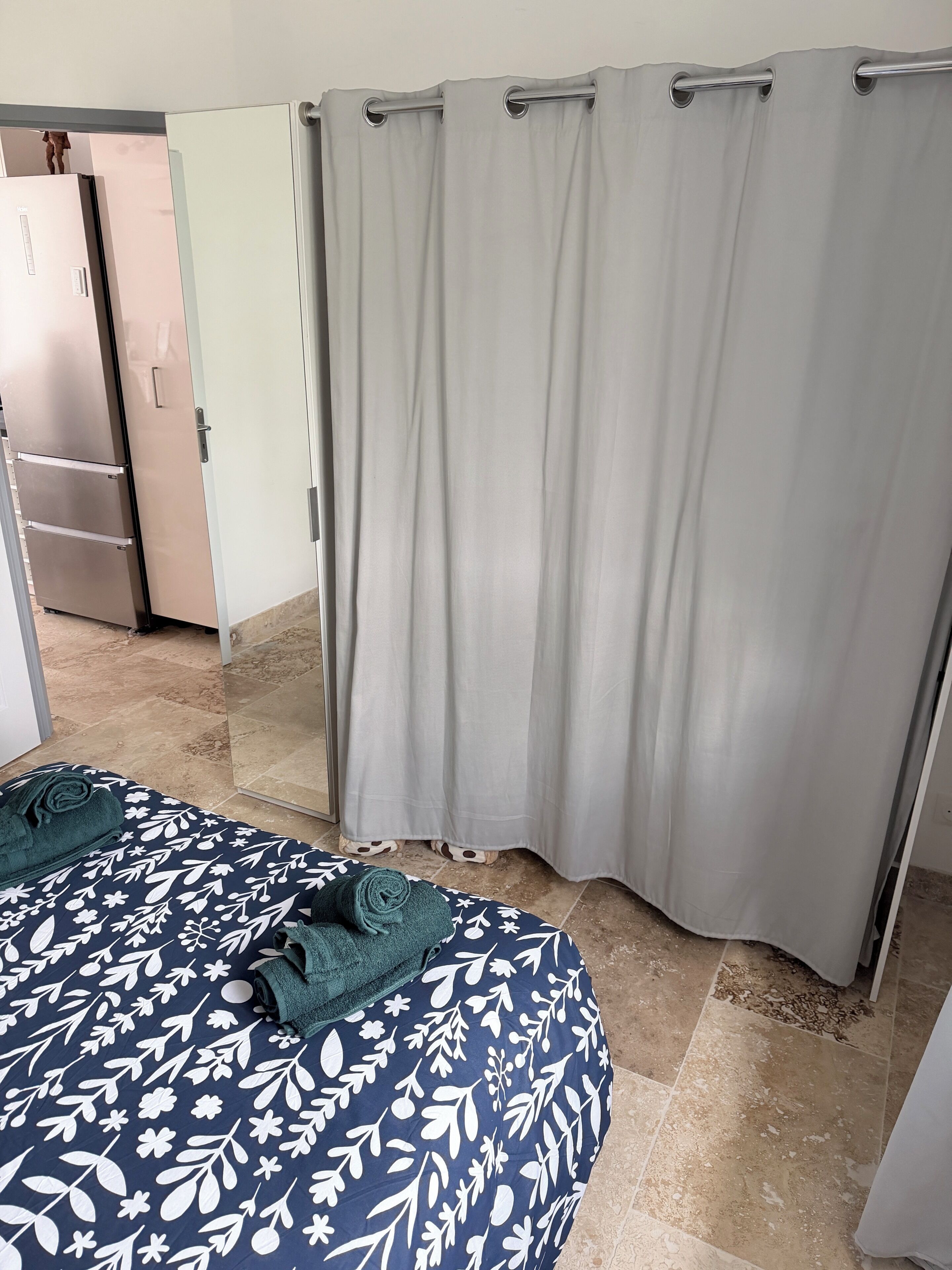 Een kamer met een bed, gordijn, spiegel en een koelkast.