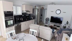 Eine moderne Küche mit integrierten Geräten, ein Essbereich mit rundem Tisch und ein Wohnbereich mit Sofa und Fernseher.