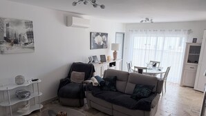 Ein Wohnzimmer mit Sofa, Sessel, Couchtisch und einem Essbereich mit Tisch und Stühlen.