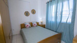 Ein Schlafzimmer mit Bett, Nachttisch, Lampe und einem Fenster mit Vorhängen.