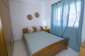 A bedroom with a bed, a nightstand, a lamp, and a window with curtains.