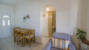 Ein Zimmer mit Esstisch und Stühlen, einem Sofa, einer kleinen Pflanze und einer Tür zu einem anderen Raum.