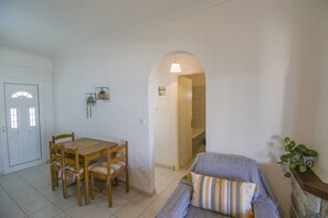 A room with a dining table and chairs, a sofa, a small plant, and a doorway leading to another room.