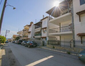 A residential street with multi-story buildings, parked cars, and a clear sky.