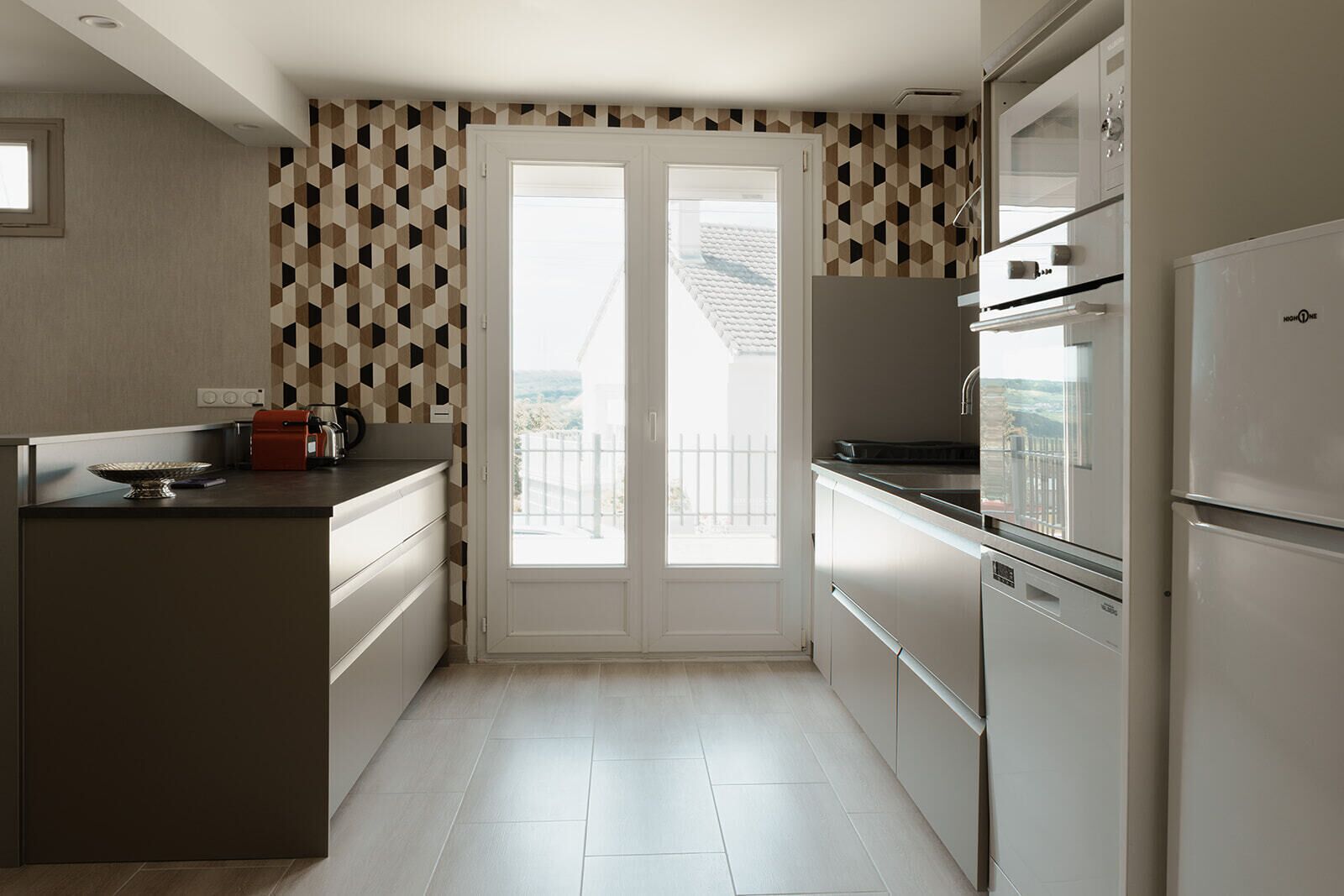 A modern kitchen with a central island, a built-in oven, and a large window overlooking a balcony.