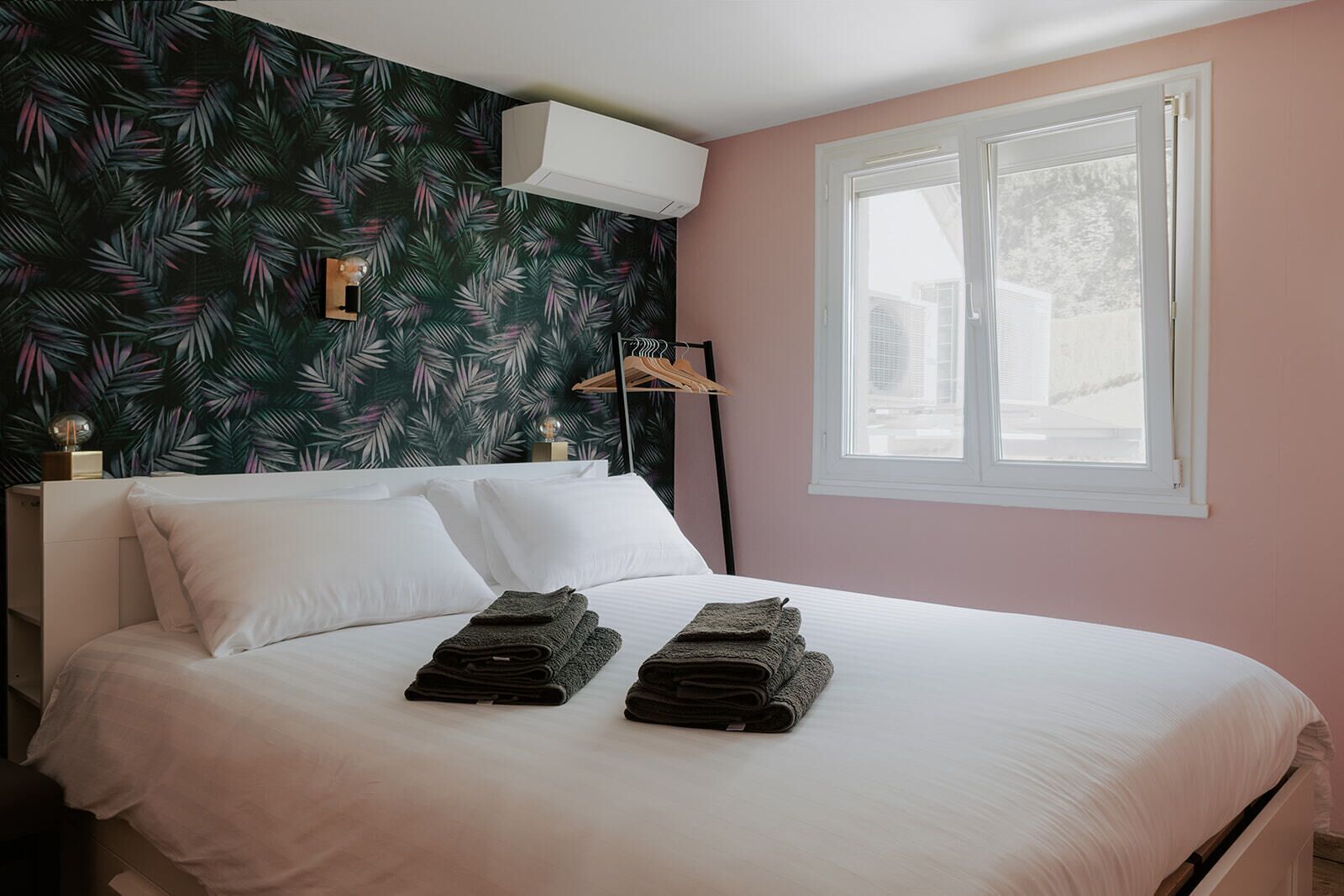 A bedroom with a bed, pillows, a window, and a wall air conditioner.