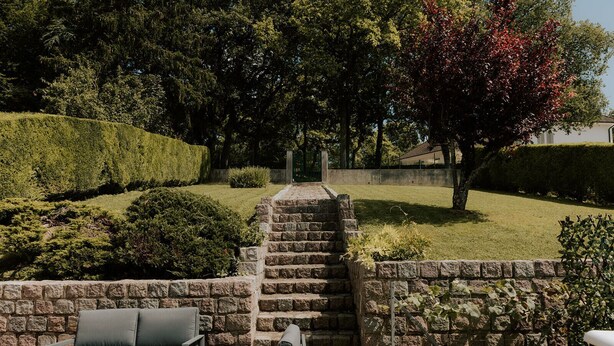 Un escalier en pierre menant à un cimetière, entouré de haies et d’arbres bien entretenus.