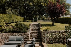 Un escalier en pierre menant à un cimetière, entouré de haies et d’arbres bien entretenus.