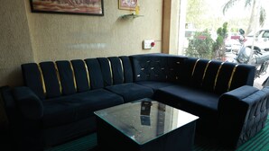 A dark-colored sofa with gold accents, a glass-top coffee table, and a green carpeted floor.