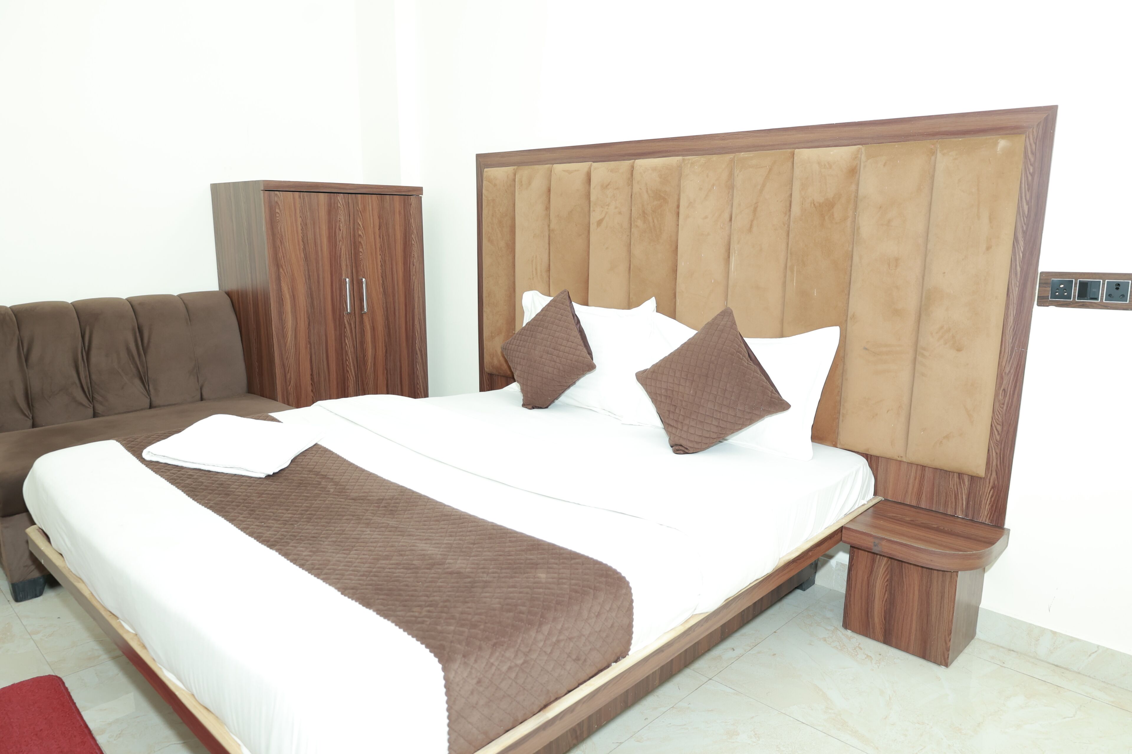 Een hotelkamer met een bed, een houten garderobe en een bruine bank.