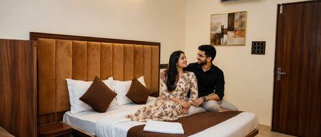 A hotel room with a large bed, a wooden headboard, an air conditioning unit, and a door.