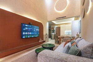 Una sala de estar moderna con un televisor de pantalla plana montado en la pared, un sofá, una mesa de centro y una zona de cocina al fondo.