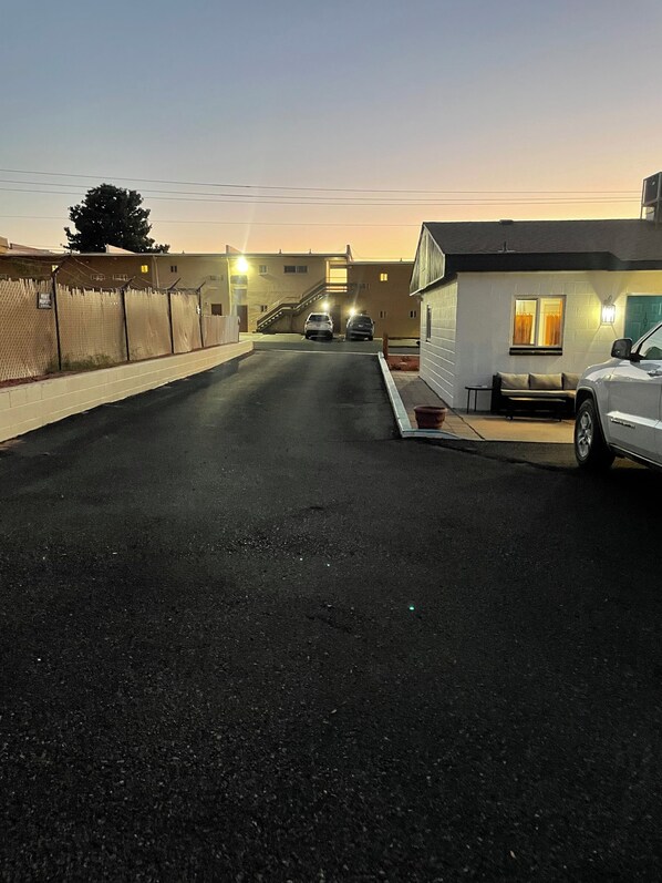 A parking lot with two cars, a fenced area, and a building with a light on the right.