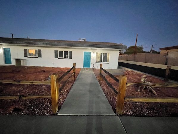 A house with a concrete pathway leading to the front door, a small table, and a blue door.