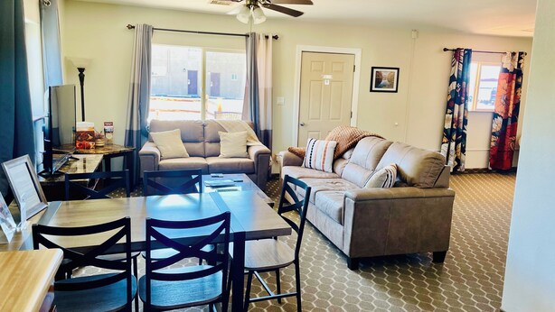 A living room with a sofa, a dining table with chairs, a ceiling fan, and a window with curtains. - Awesome 1-bedroom apartment with AC in charming Page (Page)