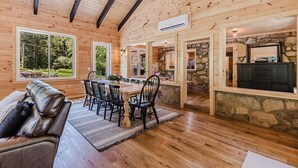 A wooden cabin interior with a dining area, kitchen, and a stone fireplace. - 6BR 63 Acre Park Like Estate Loud Creek Trails Pond Huge Yard Pickleball Golf (Whittier)