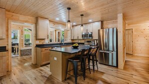 A modern kitchen with wooden cabinetry, a central island with bar stools, stainless steel appliances, and pendant lighting. - 6BR 63 Acre Park Like Estate Loud Creek Trails Pond Huge Yard Pickleball Golf (Whittier)