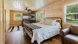 A wooden cabin bedroom with a bed, a chair, a ceiling fan, and a window with blinds. - 6BR 63 Acre Park Like Estate Loud Creek Trails Pond Huge Yard Pickleball Golf (Whittier)