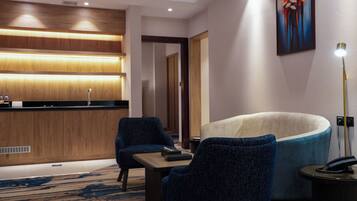 Un vestíbulo de hotel con mostrador de recepción, dos sillones, un sofá, una lámpara y un cuadro en la pared.