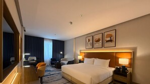 Habitación de hotel con una cama grande, un escritorio, una silla, una mesita de noche con lámpara y un espejo amplio.