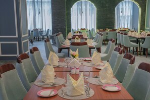 A dining area with round tables, chairs, and neatly set tables with napkins, glasses, and cutlery.