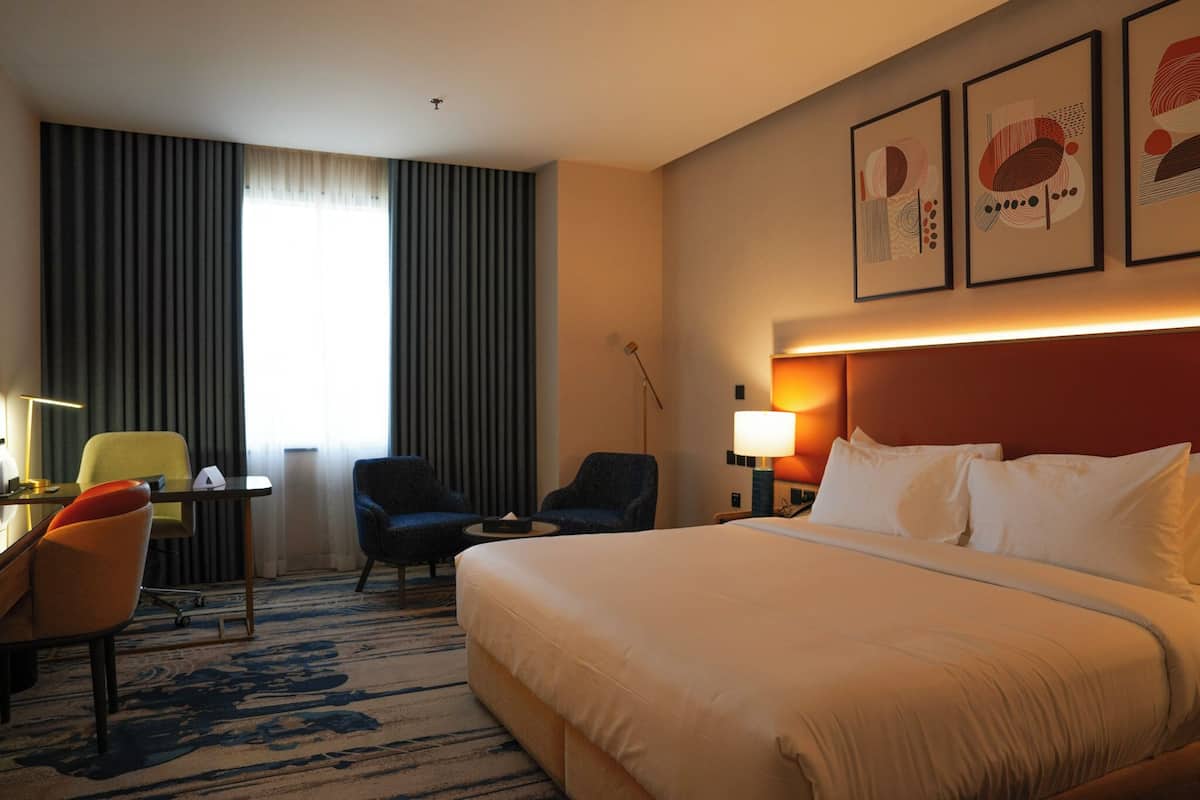 A hotel room with a bed, two armchairs, a desk, a lamp, and a window with curtains.