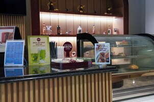 Un présentoir Costa Coffee avec un menu, une enseigne indiquant le type de café, et une vitrine réfrigérée contenant des pâtisseries.