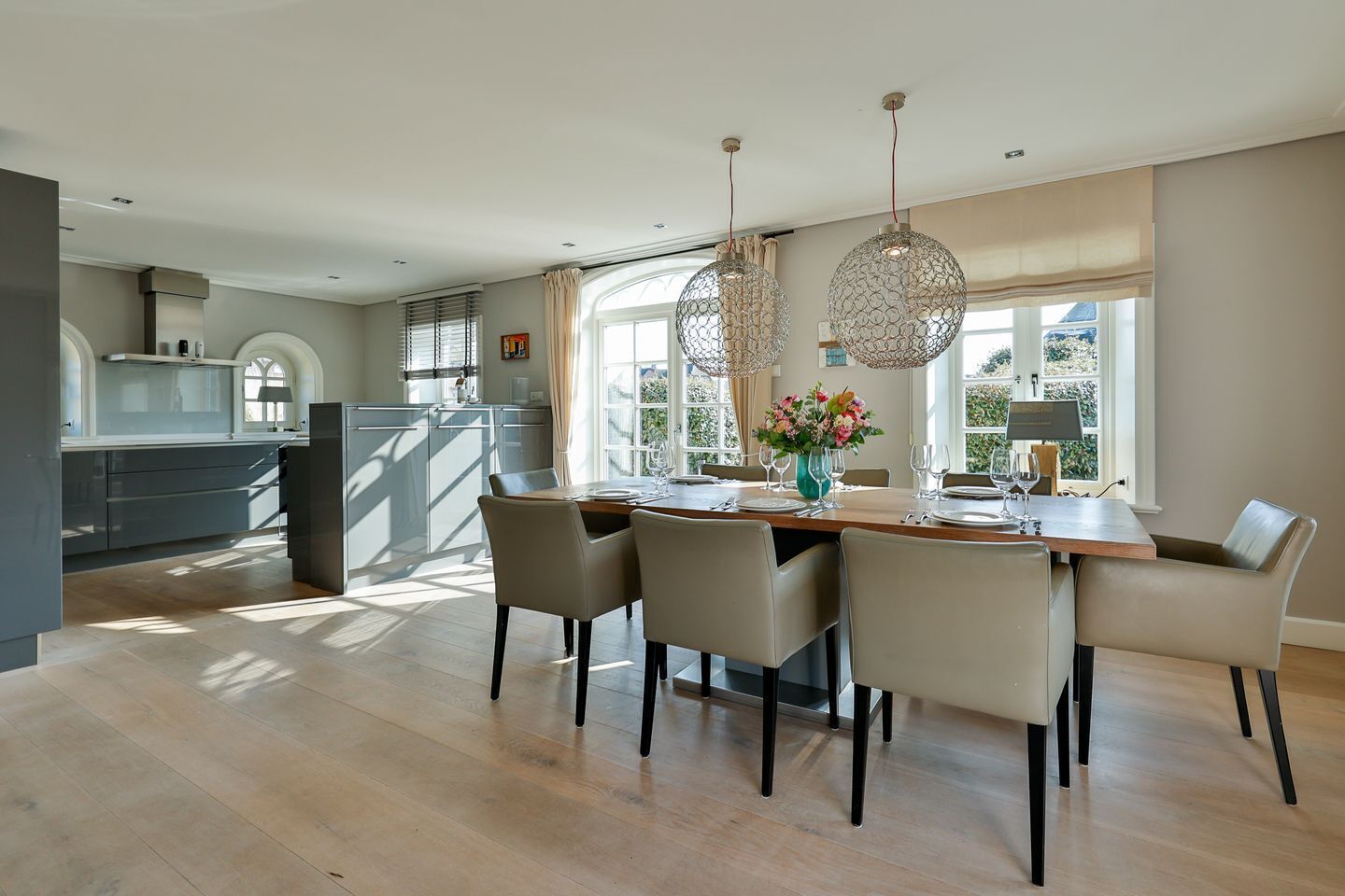 A modern kitchen with a dining area, large windows, and a view of greenery.