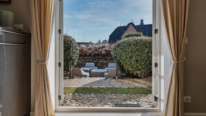 En åben dør fører ud til en patio med en stensti, et siddeområde og et hus i baggrunden.