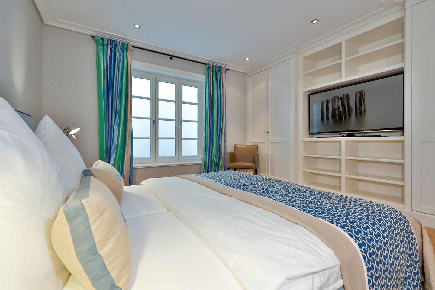 Un dormitorio con cama, televisor, silla y ventana con cortinas.