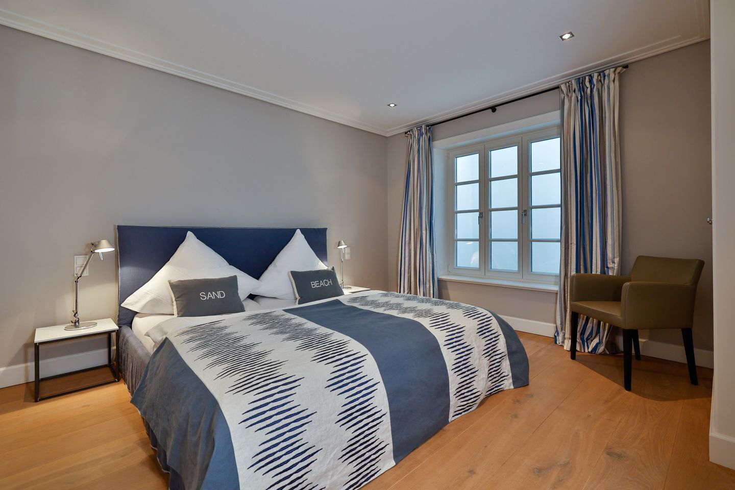 A bedroom with a bed, nightstands, a chair, a window with curtains, and a view.