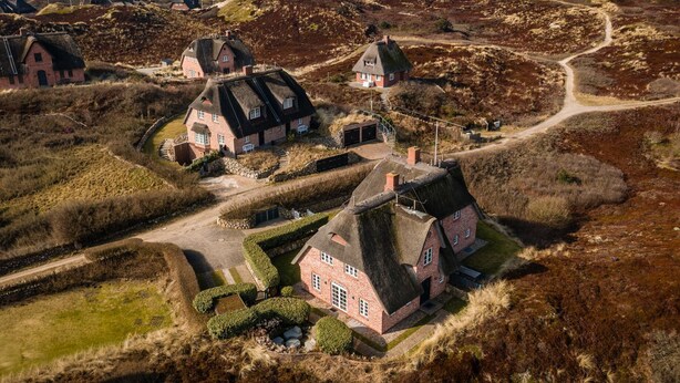 Landskab med bindingsværkshuse, en snoet sti og et vandareal i det fjerne.