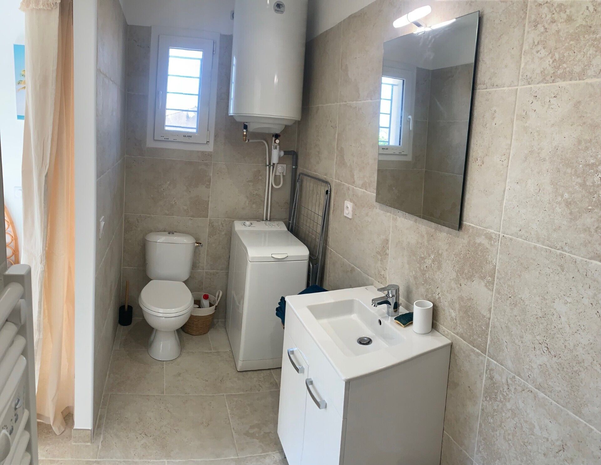 Une petite salle de bain comprenant des toilettes, un lave-linge, un lavabo et un miroir.