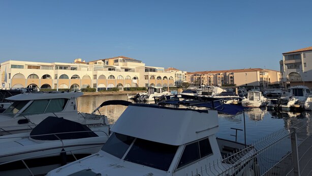 Marina com barcos atracados, um edifício com janelas em arco e céu claro.