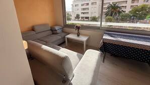 Um apartamento moderno com um sofá cinzento, uma pequena mesa branca e uma toalha de mesa estampada.