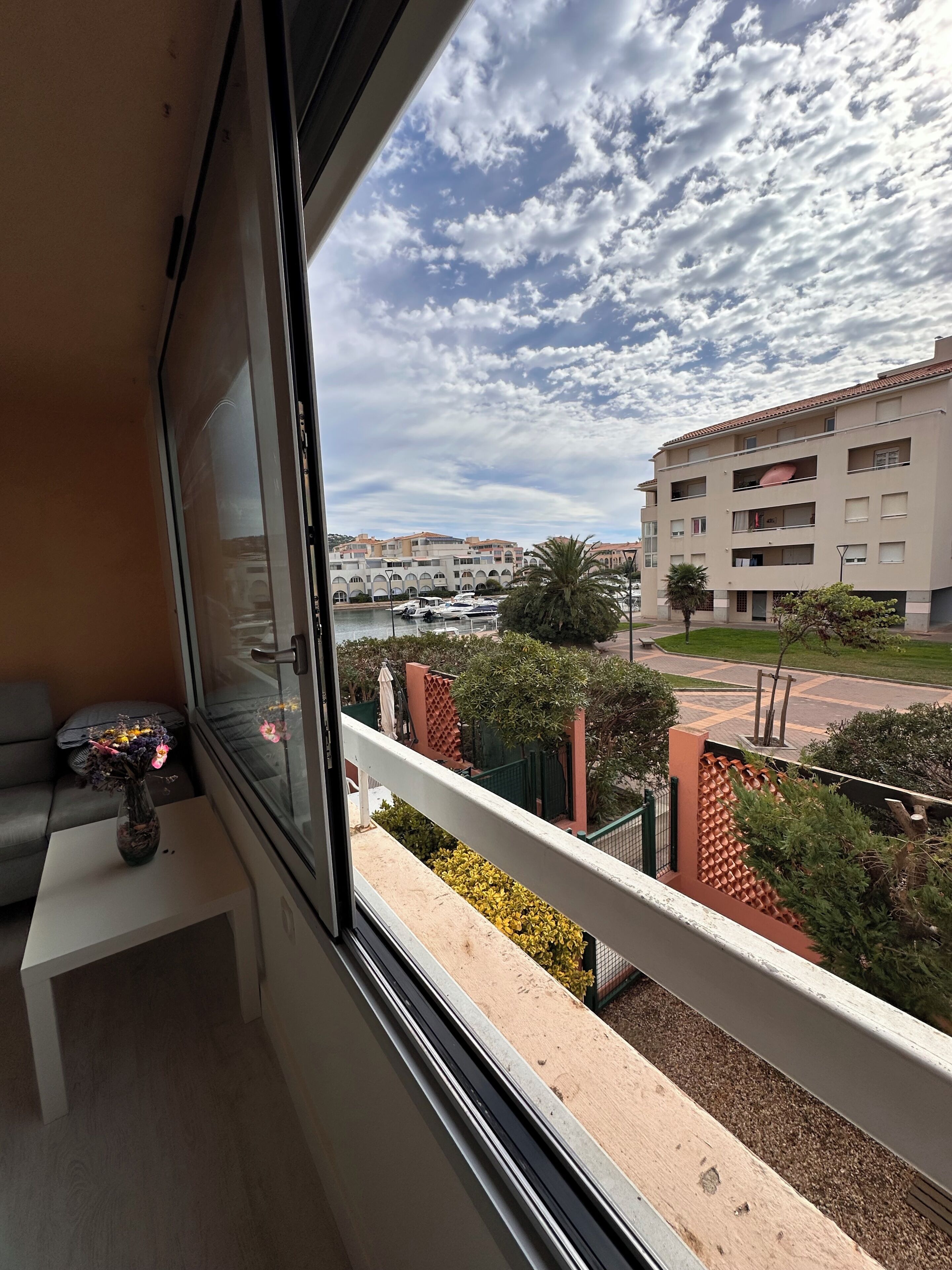 A balcony with a view of a marina, a building with balconies, and a small table with a vase.