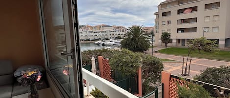 A balcony with a view of a marina, a building with balconies, and a small table with a vase.