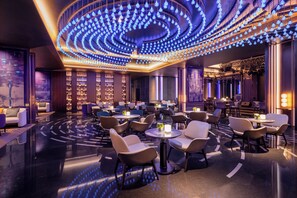 Un hall d’hôtel moderne doté d’un luminaire circulaire au plafond, d’espaces aménagés pour s’asseoir et d’un bar.
