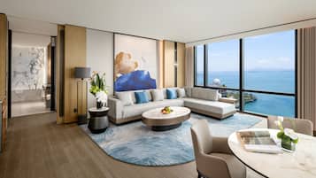 Una habitación de hotel moderna con un ventanal grande, un sofá, una mesa de centro y vistas al mar.